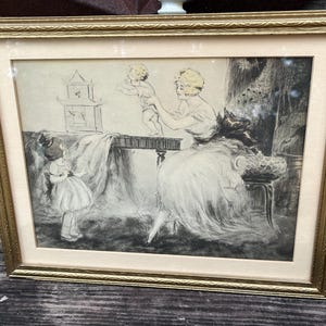 May include: A framed black and white print featuring a seated figure holding a small child on a table, with another child standing nearby. The scene includes a birdcage in the background. The artwork is enclosed in a textured gold-colored frame.