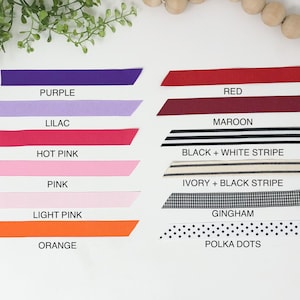 May include: A collection of ribbon samples in various colors and patterns, including purple, lilac, red, maroon, hot pink, pink, light pink, orange, black and white stripe, ivory and black stripe, gingham, and polka dots.