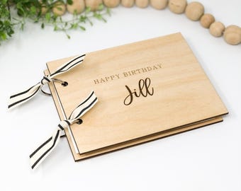 Könnte beinhalten: Ein Holzfotoalbum mit einer schwarzen und weißen Schleifenverschlusses. Der Deckel ist mit dem Text "Happy Birthday Jill" graviert.