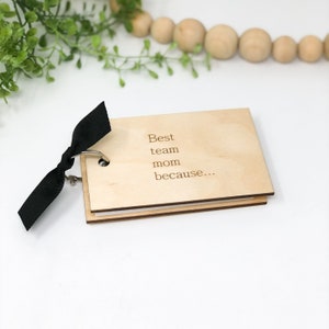 May include: A small wooden book with a black ribbon tied around it. The cover has the text "Best team mom because..." engraved on it.