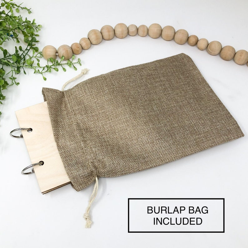 May include: A wooden ring binder with silver rings, partially inside a brown burlap bag with a drawstring. The text "Burlap Bag Included" is printed in white on a black rectangle below the image.