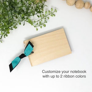 May include: A wooden notebook with a teal and black ribbon tied around it. Customize your notebook with up to 2 ribbon colors.