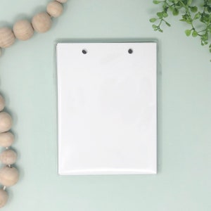May include: A white sheet of paper with two black dots in the top corners, inside a clear plastic sleeve.