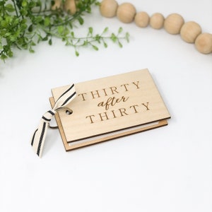 May include: A wooden guest book with a black and white ribbon. The cover is engraved with the text "Thirty after Thirty".
