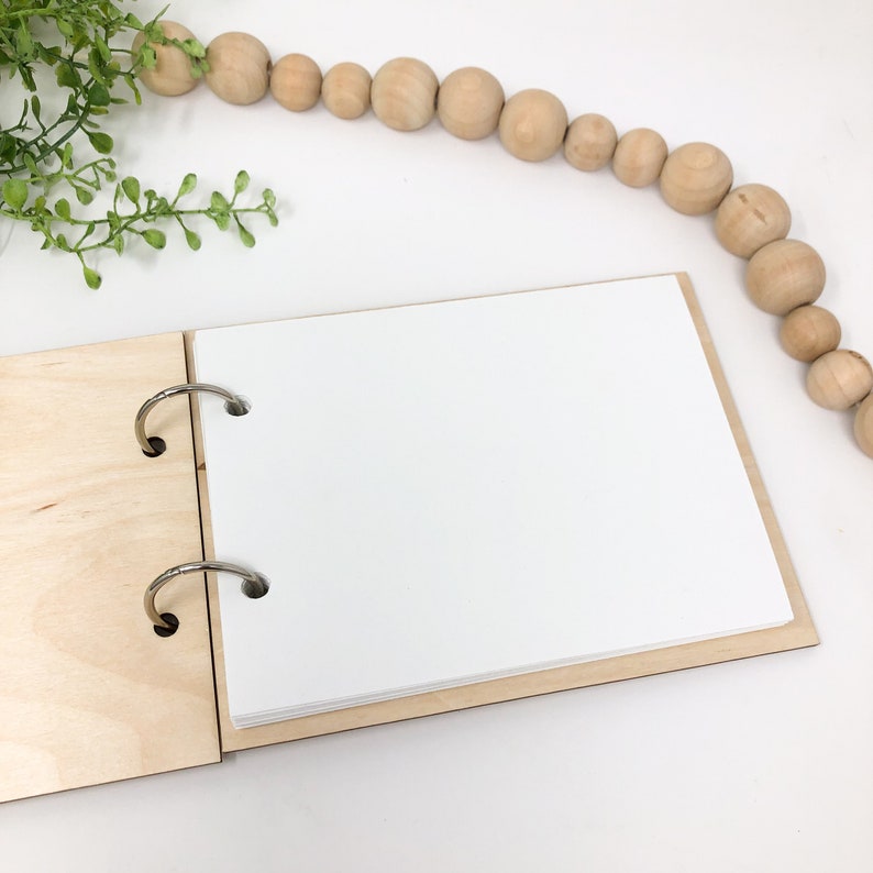 May include: A wooden photo album with a white paper insert and two silver rings. The album is open and the paper insert is blank.