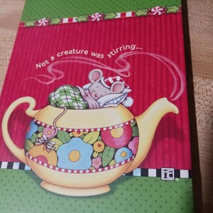 May include: A decorative notebook with a red background and the text "Not a creature was stirring...". The notebook features a yellow teapot with floral designs and a sleeping mouse wearing a nightcap. The top border is green with candy cane designs.