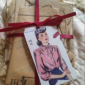 May include: A stack of vintage sewing patterns tied with a red ribbon. The pattern is for a blouse with a red and white striped design. The pattern size is 14 and 32.