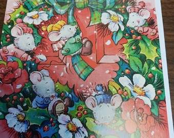 May include: A Christmas card featuring a wreath with white mice wearing winter clothing. The wreath is decorated with red roses, white flowers, green holly, and a plaid bow. The background is a soft red.