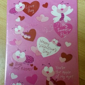 May include: A sheet of Valentine's Day stickers featuring cartoon bug characters and heart shapes in shades of pink, red, and white. Text includes phrases like "Love Bug," "Be Mine," and "Happy Valentine's Day!"