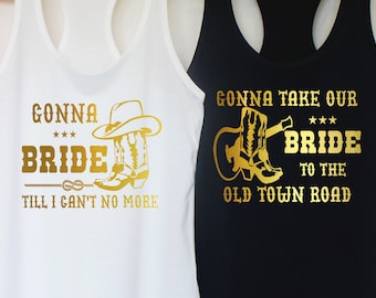 Puede incluir: Tres camisetas sin mangas con un diseño de purpurina dorada que dice "Gonna take our bride to the old town road". Las camisetas sin mangas son rosa, blanca y negra.