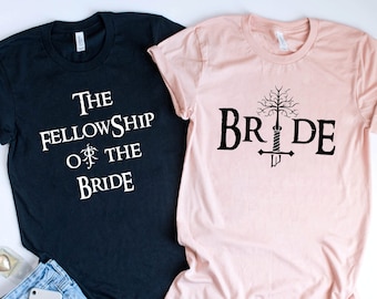 May include: Two t-shirts, one black and one pink, with a Lord of the Rings theme. The black shirt says "The Fellowship of the Bride" and the pink shirt says "Bride" with a tree and sword graphic.