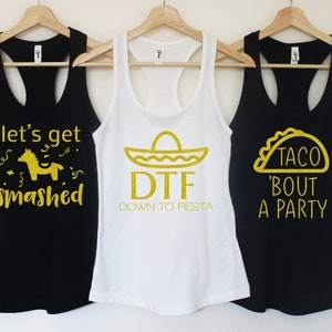 Puede incluir: Tres camisetas de tirantes negras con texto de purpurina dorada. La primera camiseta de tirantes dice "Let's get smashed" con una pi&ntilde;ata dorada de purpurina. La segunda camiseta de tirantes dice "DTF Down to Fiesta" con un sombrero dorado de purpurina. La tercera camiseta de tirantes dice "Taco 'bout a party" con un taco dorado de purpurina.