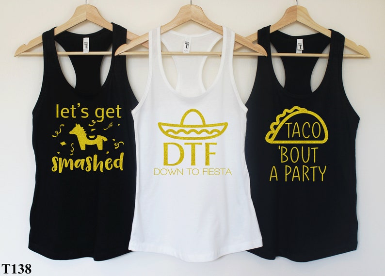 Puede incluir: Tres camisetas de tirantes negras con texto de purpurina dorada. La primera camiseta de tirantes dice "Let's get smashed" con una pi&ntilde;ata dorada de purpurina. La segunda camiseta de tirantes dice "DTF Down to Fiesta" con un sombrero dorado de purpurina. La tercera camiseta de tirantes dice "Taco 'bout a party" con un taco dorado de purpurina.