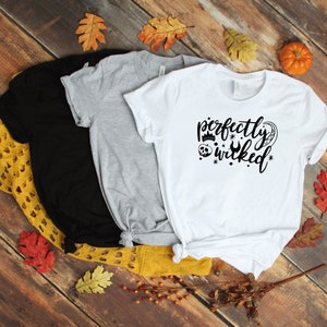 May include: Three t-shirts with different colors, black, gray, and white. The white t-shirt has a black graphic that says "perfectly wicked" with a crown, skull, and a wrench.