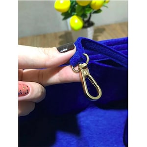 May include: A close-up of a blue velvet bag with a gold metal hook. The hook is attached to the bag with a loop of fabric.