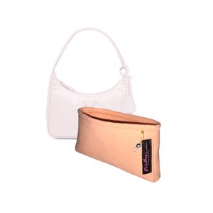 Puede incluir: Un bolso de mano rosa pálido con una correa corta y un pequeño borla. El bolso está forrado con un organizador de bolso de fieltro color melocotón con una etiqueta negra que dice "Felt Bag Organizer by Creative Expressions".