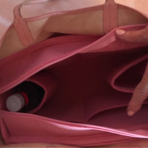 Puede incluir: Una bolsa de lona rosa con cierre de cremallera en la parte superior y varios compartimentos. La bolsa est&aacute; abierta y muestra una botella dentro de uno de los compartimentos.