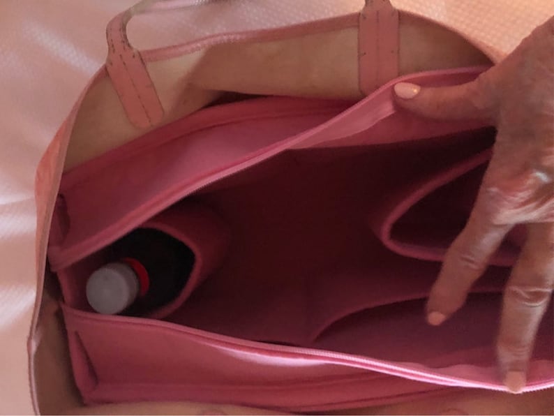 Puede incluir: Una bolsa de lona rosa con cierre de cremallera en la parte superior y varios compartimentos. La bolsa est&aacute; abierta y muestra una botella dentro de uno de los compartimentos.