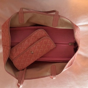 Puede incluir: Una bolsa de mano rosa con un bolsillo con cremallera y una bolsa m&aacute;s peque&ntilde;a de color rosa con estampado en su interior. La bolsa tiene un asa superior y un cierre de cremallera.