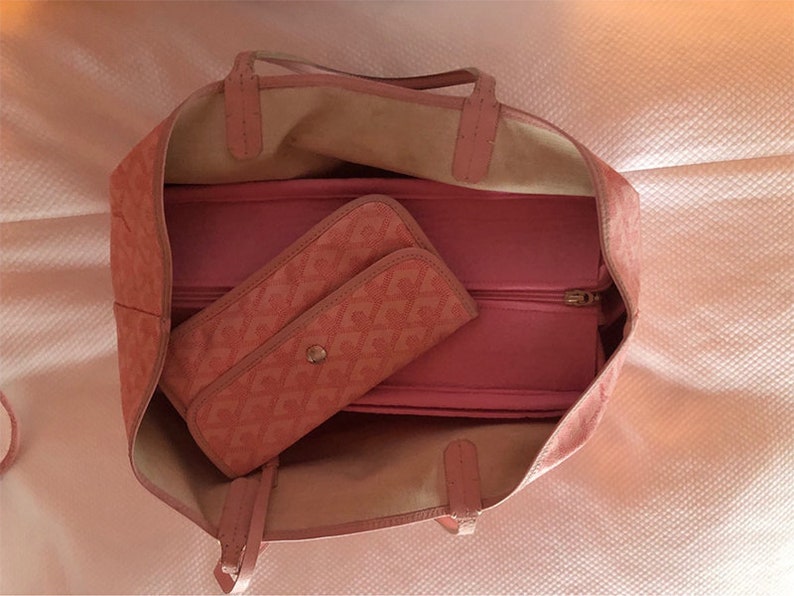 Puede incluir: Una bolsa de mano rosa con un bolsillo con cremallera y una bolsa m&aacute;s peque&ntilde;a de color rosa con estampado en su interior. La bolsa tiene un asa superior y un cierre de cremallera.