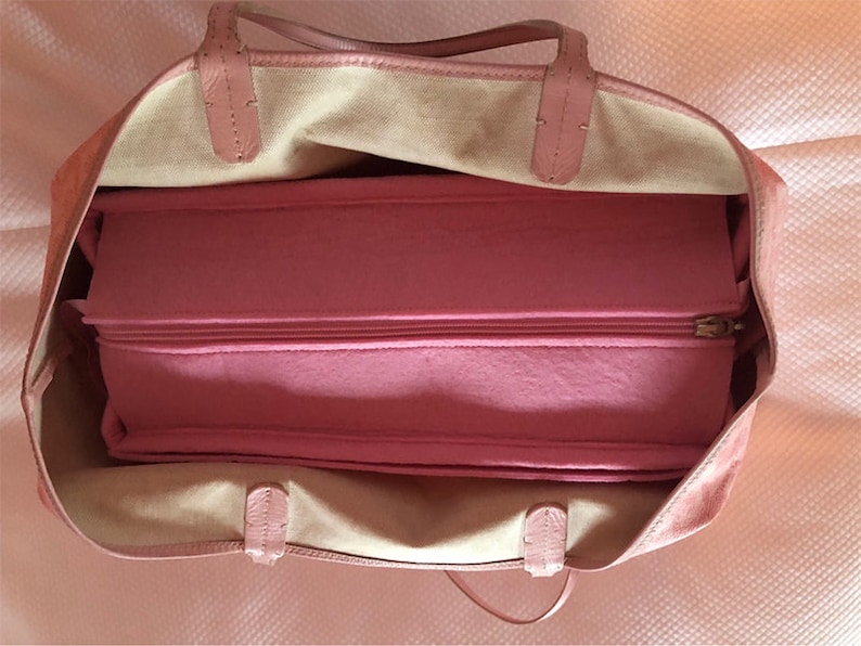 Puede incluir: Una bolsa de mano rosa con un compartimento con cremallera en el interior. La bolsa est&aacute; hecha de un material suave y texturizado y tiene un dise&ntilde;o sencillo.