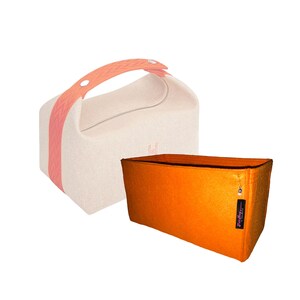 Könnte beinhalten: Eine beigefarbene Stofftasche mit einem korallenfarbenen Griff mit Zickzackmuster sowie ein separater rechteckiger Filz-Organizer in Orange mit einem kleinen schwarzen Etikett und einem dekorativen augenförmigen Anhänger.