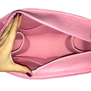 Puede incluir: Organizador de bolso de fieltro rosa con m&uacute;ltiples compartimentos y cierre de cremallera. La bolsa est&aacute; abierta y el interior es visible.