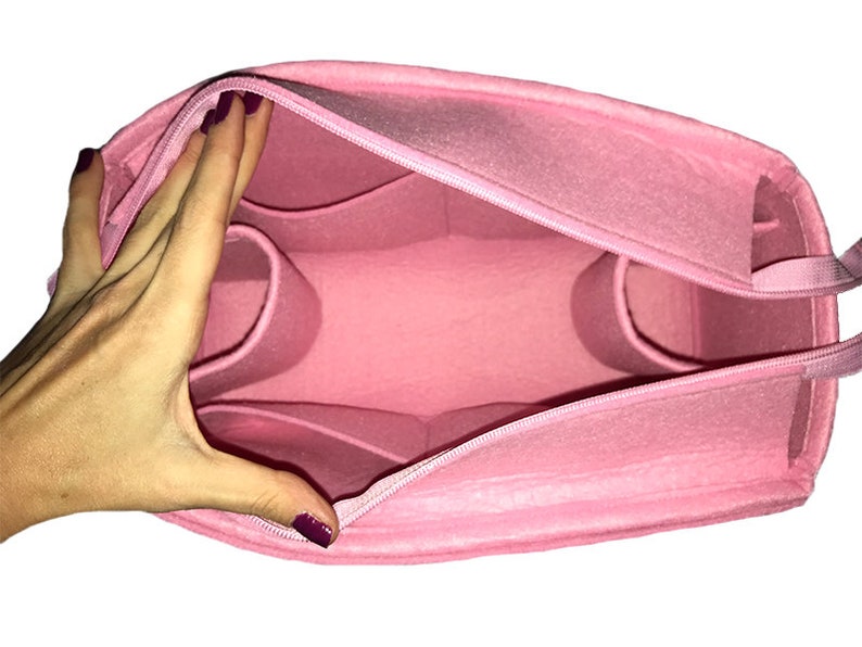 Puede incluir: Organizador de bolso de fieltro rosa con m&uacute;ltiples compartimentos y cierre de cremallera. La bolsa est&aacute; abierta y el interior es visible.