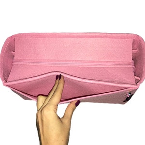 Puede incluir: Un organizador de bolso de fieltro rosa con un compartimento con cremallera y varios bolsillos. El organizador est&aacute; dise&ntilde;ado para caber dentro de un bolso m&aacute;s grande.
