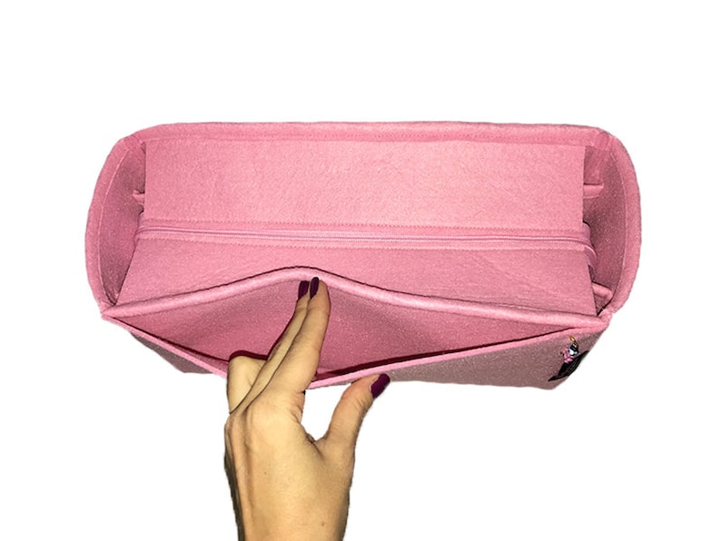 Puede incluir: Un organizador de bolso de fieltro rosa con un compartimento con cremallera y varios bolsillos. El organizador est&aacute; dise&ntilde;ado para caber dentro de un bolso m&aacute;s grande.