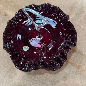 Könnte beinhalten: Ein rubinrotes Serviergeschirr aus Glas mit gerüschtem Rand und einem silbernen Griff. Das Geschirr hat eine runde Form und einen kleinen, runden Aufkleber. Der Griff ist in der Mitte des Geschirrs befestigt.