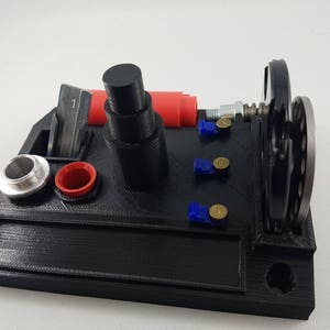 May include: A black 3D printed tool holder with a red and silver component, a black wheel, and blue and silver accents.