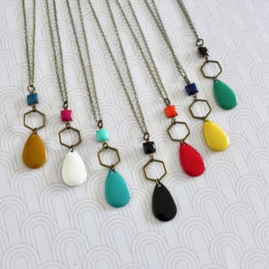 Peut inclure: Sept colliers avec des pendentifs géométriques. Chaque collier présente un pendentif en forme de larme de couleur différente et un charme hexagonal. Les pendentifs sont dans des tons turquoise, rouge, jaune, blanc, noir, vert et marron.
