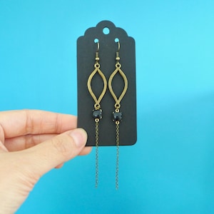 Peut inclure: Une paire de boucles d'oreilles longues et pendantes avec une pierre précieuse noire et un motif en forme de feuille de couleur or.