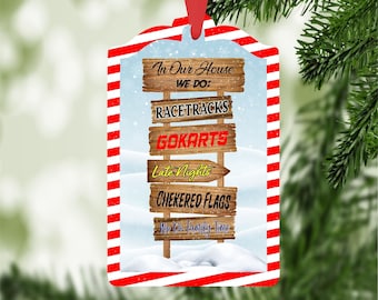 May include: A Christmas bauble with a red and white striped background. The bauble features a wooden sign with the text "In Our House We Do: Racetracks, Gokarts, Late Nights, Checkered Flags, We Do Family Time".