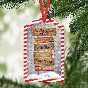 May include: A Christmas ornament shaped like a wooden sign with the text "In This House We Do: Burn-Outs, Fast Cars, Win Lights, Drag Racing, We Do Family Time". The sign is decorated with a red and white striped border and a silver background.
