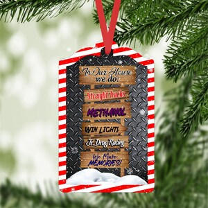 May include: A red and white striped Christmas ornament with a black metal background. The ornament features a series of wooden signs with the text "In Our House we do: Straight Tracks, Methanol, Win Lights, Jr. Drag Racing, We Make Memories!"