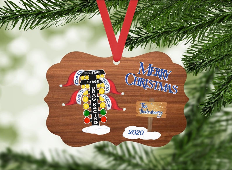 May include: A wooden Christmas ornament featuring a drag racing Christmas tree with red, green, and yellow lights. The ornament has the names "Dad", "Johnny Ty", "Tracey", and "Nick" on it. The ornament also has the text "Merry Christmas" and "The Hedenburgs" on it. The year "2020" is also on the ornament.