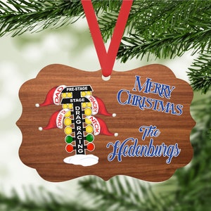 May include: A wooden Christmas ornament with a drag racing Christmas tree light display. The ornament is decorated with red and green lights, and the text "Merry Christmas The Hedenburgs" is written in blue on the ornament.