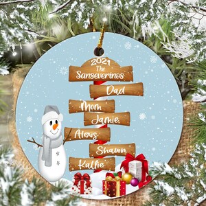 May include: A round Christmas ornament with a blue background and a snowman. The ornament features a candy cane with wooden signs that read "2021 The Sanseverinos", "Dad", "Mom", "Jamie", "Alexis", "Shawn", and "Kallie".