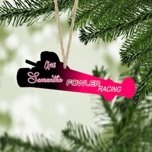 May include: A pink and black Christmas ornament shaped like a race car with the text "#18 Samantha Fowler Racing" on it.