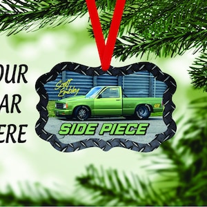 May include: A green truck with a black and silver metal ornament. The ornament has a diamond pattern and the words "Side Piece" in green letters. The truck is in front of a gray metal fence.