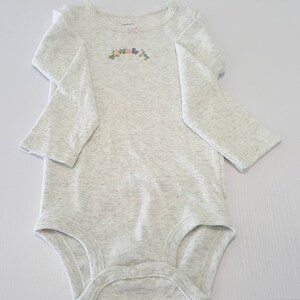 May include: A gray long-sleeved bodysuit with a floral design on the front.