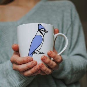 a woman holding a coffee cup with a blue bird on it