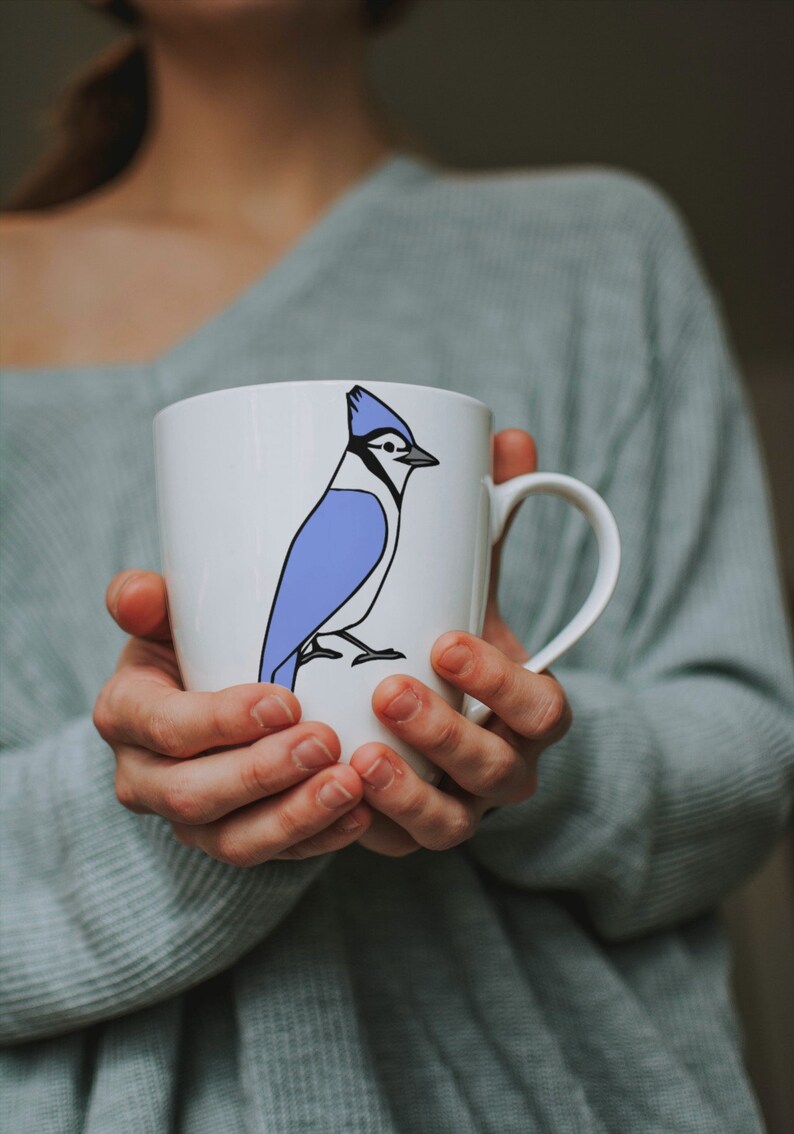 a woman holding a coffee cup with a blue bird on it