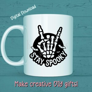 May include: White ceramic mug with a black graphic of a skeleton hand making a rock-and-roll gesture, with the words "STAY SPOOKY" and bats. The words "Digital Download" and "Make creative DIY gifts!" are also visible.