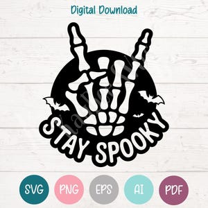 May include: Black and white Halloween-themed graphic with a skeleton hand making a rock-and-roll gesture. The words "STAY SPOOKY" are in a stylized font. Includes digital download file type icons: SVG, PNG, EPS, AI, and PDF.