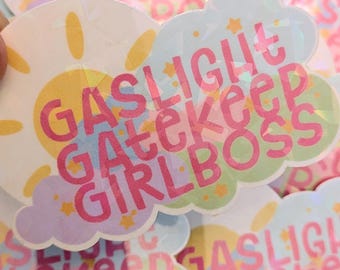 May include: A pastel pink, blue, and green sticker with a cloud shape and the text "Gaslight Gatekeep Girlboss" in pink letters. The sticker has a holographic finish.