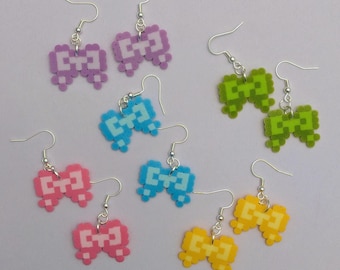Op de afbeelding: Pixel-stijl strik oorbellen in verschillende kleuren: paars, groen, blauw, roze en geel. Elke paar heeft een strik ontwerp gemaakt van kleine, vierkante kralen, met zilverkleurige oorhaken. Een leuke accessoire.