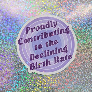 May include: A round sticker with a purple and white design. The sticker has the text "Proudly Contributing to the Declining Birth Rate" in a stylized font. The background is a shimmering, iridescent surface.